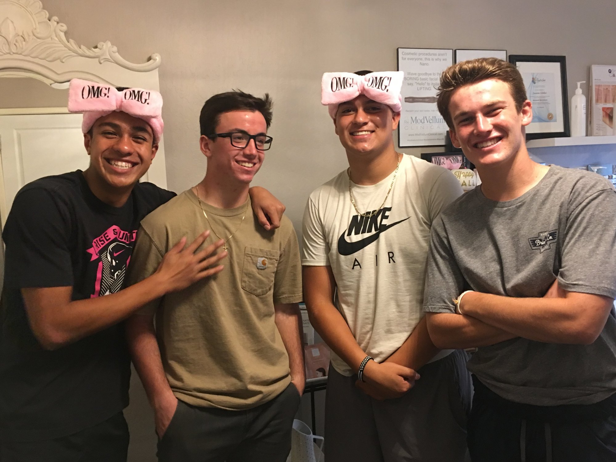 Four smiling teenage boys in “OMG” headbands after their facials at the Dermal 911 studio