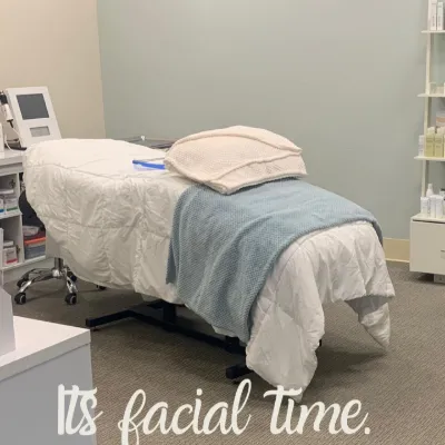 The Dermal 911 treatment room: facial bed with white linens and a blue throw